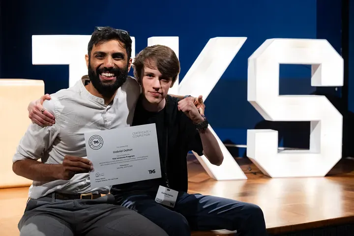 Gabriel and mentor Pranav Menon sit beside the TKS stage letters holding Gabriel’s certificate of completion.