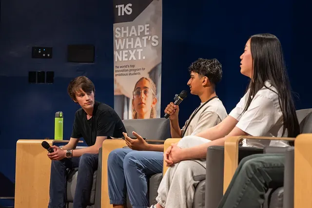 Gabriel moderates a seated panel at the TKS Vancouver Emerging Technology Showcase while another panellist speaks into a microphone.