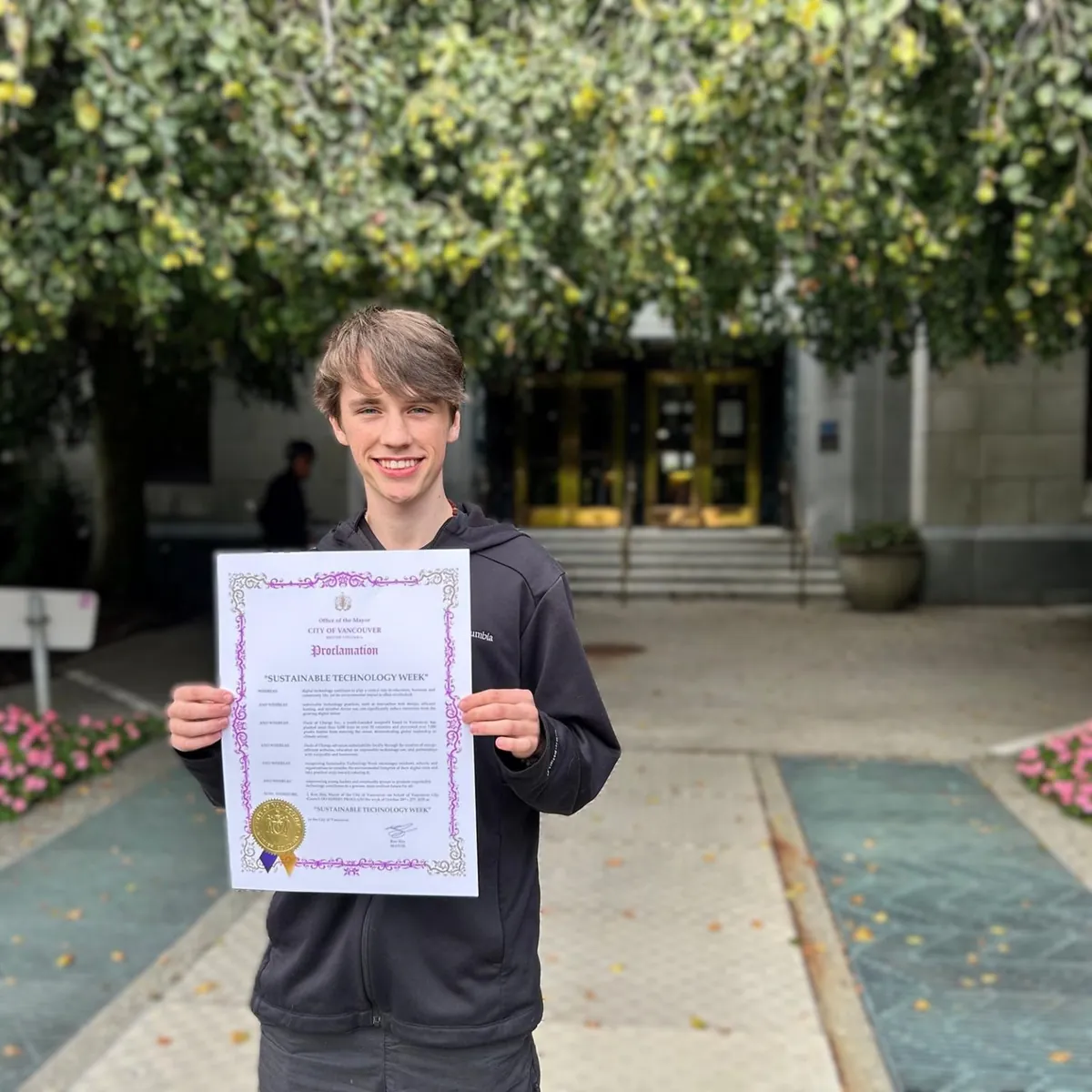 Gabriel holds the City of Vancouver’s Sustainable Technology Week proclamation outside a building entrance.