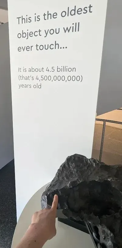 A hand touches a meteorite beside a sign saying it is about 4.5 billion years old.