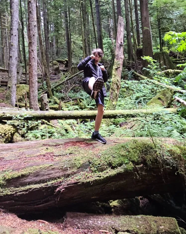 A person balances on a fallen log in the forest near Alice Lake.