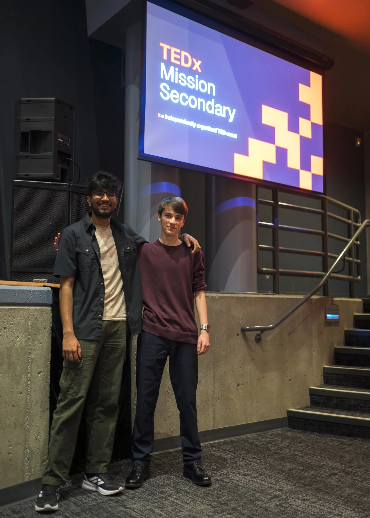 Gabriel and another person stand beneath a screen reading “TEDx Mission Secondary” at the event.