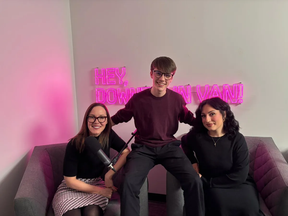 Gabriel sits between Jane Talbot and Sofia Laratta beneath the “Hey, Downtown Van!” sign in the podcast studio.