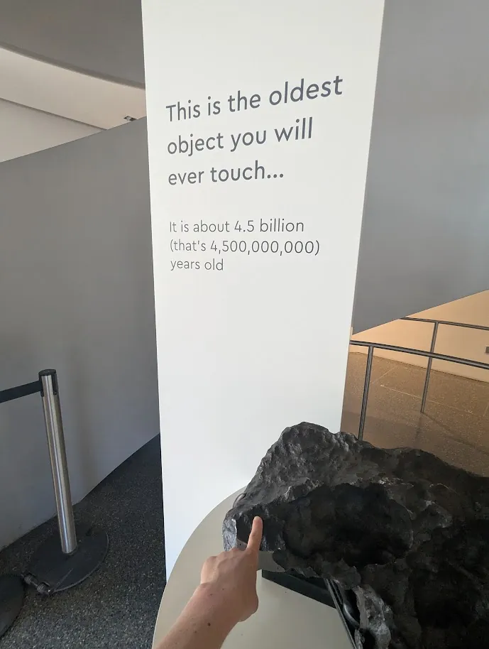 A hand touches a meteorite beside a sign saying it is about 4.5 billion years old.
