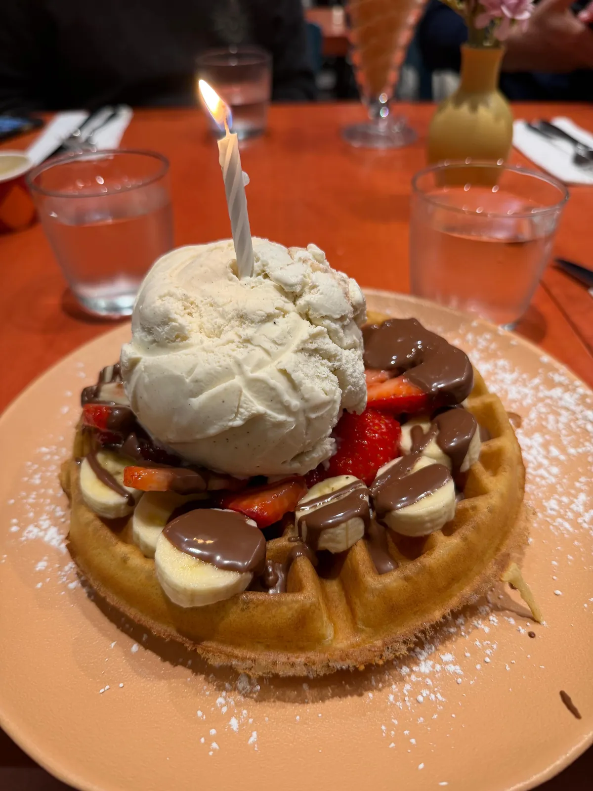 A birthday candle burns above ice cream, fruit and chocolate on a waffle for Gabriel’s eighteenth birthday.