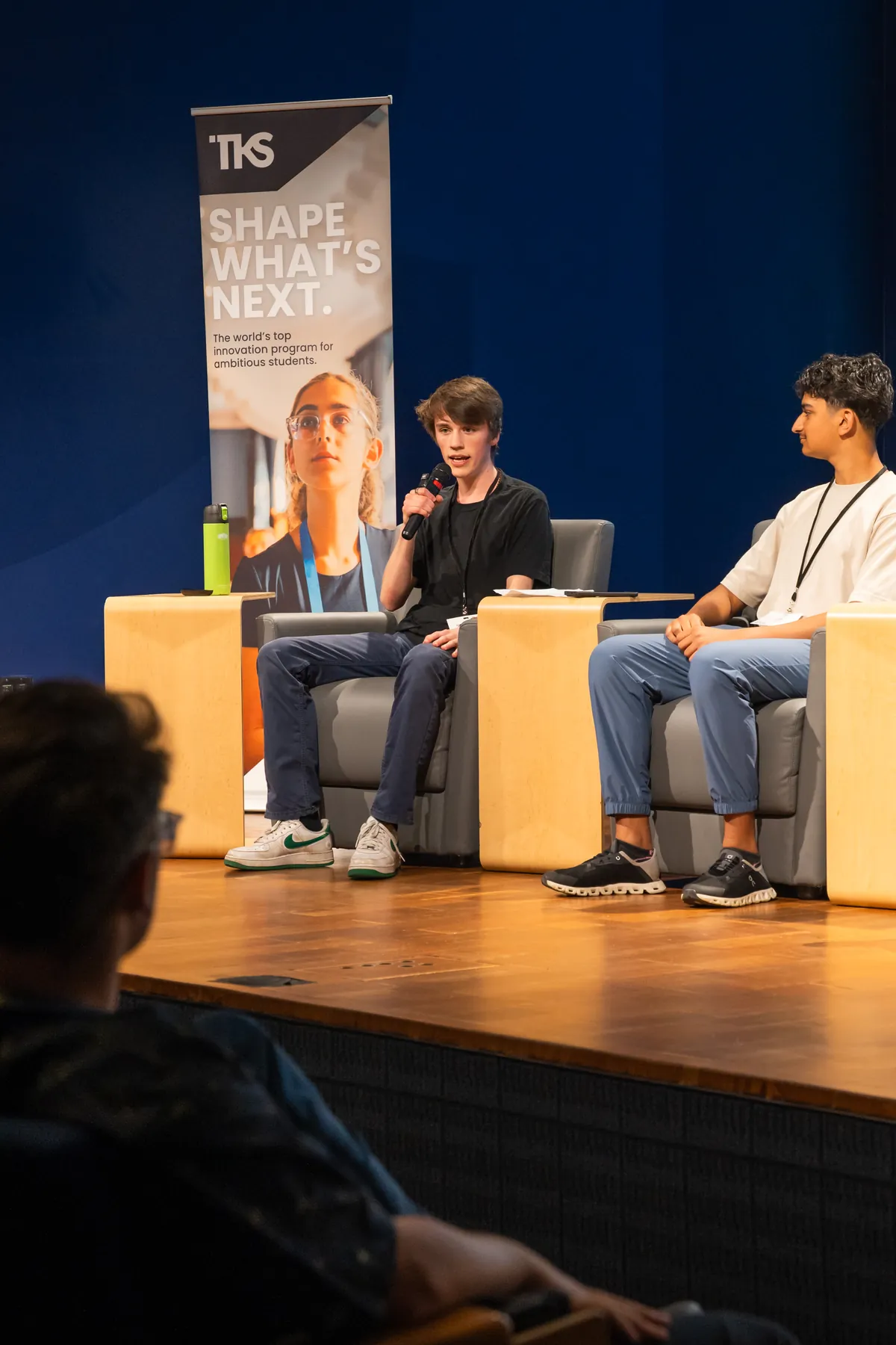 Gabriel speaks into a microphone beside another panellist at the TKS Vancouver Showcase.