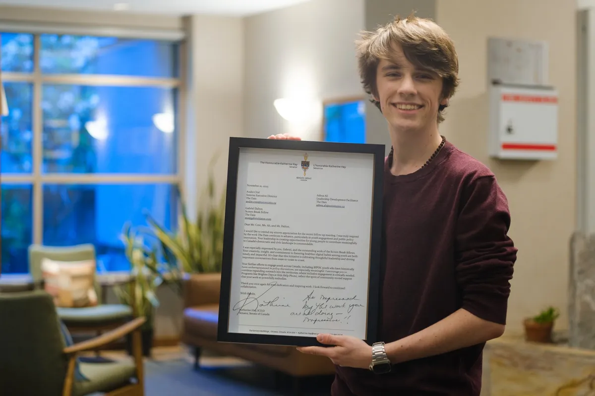 Gabriel holds a framed letter from Senator Katherine Hay recognizing his work with The Dais’ Screen Break program.