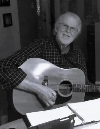 Gabriel’s grandfather smiles while holding an acoustic guitar in a black-and-white portrait.